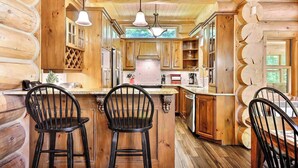 A log cabin interior with a central kitchen, wooden walls, and a dining area with two chairs. - Waterfront - Family, Pool & Spa (Mille-Isles)