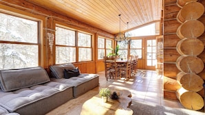 A cozy cabin interior with a wooden ceiling, large windows, a dining area, and a log wall. - Waterfront - Family, Pool & Spa (Mille-Isles)