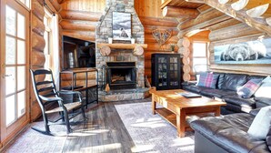 A log cabin interior with a stone fireplace, leather furniture, and wooden beams. - Waterfront - Family, Pool & Spa (Mille-Isles)