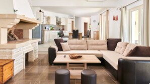 A modern living room with a sectional sofa, a fireplace, a dining area, and a kitchen in the background. - Modern Villa Melli with a pool, Whirlpool and panoramic View (Vizinada)