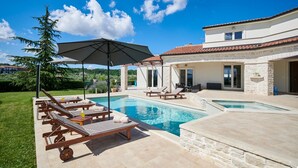 A pool area with lounge chairs and an umbrella, surrounded by a stone building with a tiled roof. - Modern Villa Melli with a pool, Whirlpool and panoramic View (Vizinada)