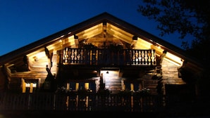 A wooden cabin with a balcony and a warm-lit interior.