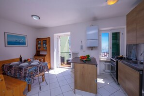 A compact kitchen with a dining area, a view through an open door, and a small island with a pot and vegetables. - Dogana Best Lake View (Nago-Torbole)