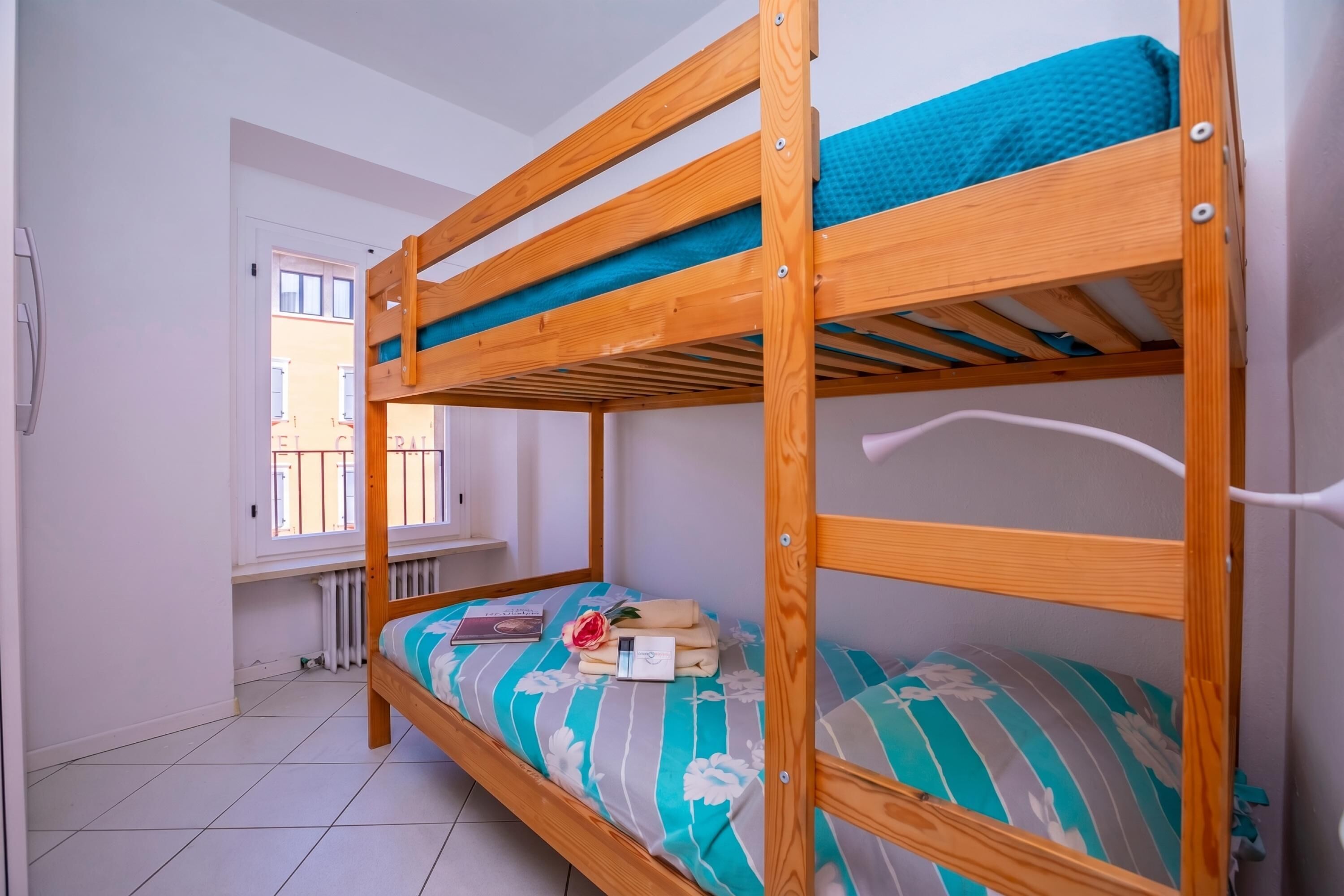 Una cama litera con colchón azul, una ventana con vistas y un radiador debajo.