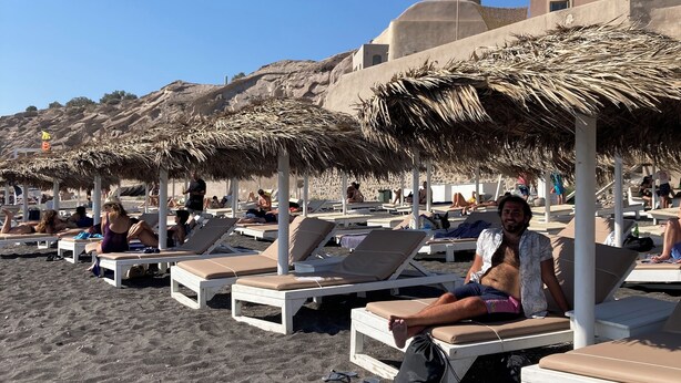 A beach with sun loungers and thatched umbrellas.