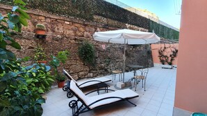 A patio with lounge chairs and a table, surrounded by potted plants and a stone wall.