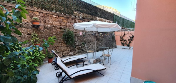 A patio with lounge chairs and a table, surrounded by potted plants and a stone wall.