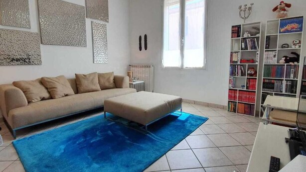A living room with a sofa, ottoman, and a bookshelf filled with books and decorative items. - 1 Bed Flat - Sleeps 2 - Parking - Wifi (San Biagio della Cima)