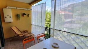 A balcony with a table, two chairs, a window with a view of greenery, and a wall-mounted air conditioning unit. - 1 Bed Flat - Sleeps 2 - Parking - Wifi (San Biagio della Cima)
