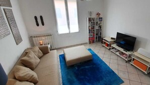 A living room with a sofa, a blue rug, a TV, a bookshelf, and a radiator. - 1 Bed Flat - Sleeps 2 - Parking - Wifi (San Biagio della Cima)