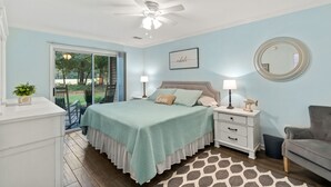 A bedroom with a bed, bedside tables, a chair, a ceiling fan, and a view of the outdoors. - Salt & Light - 1st Floor 3BR unit in True Blue (Pawleys Island)
