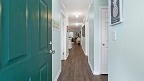 A hallway with teal walls, a wooden floor, and white doors. There is a welcome sign on the wall and a framed pineapple picture. - Salt & Light - 1st Floor 3BR unit in True Blue (Pawleys Island)