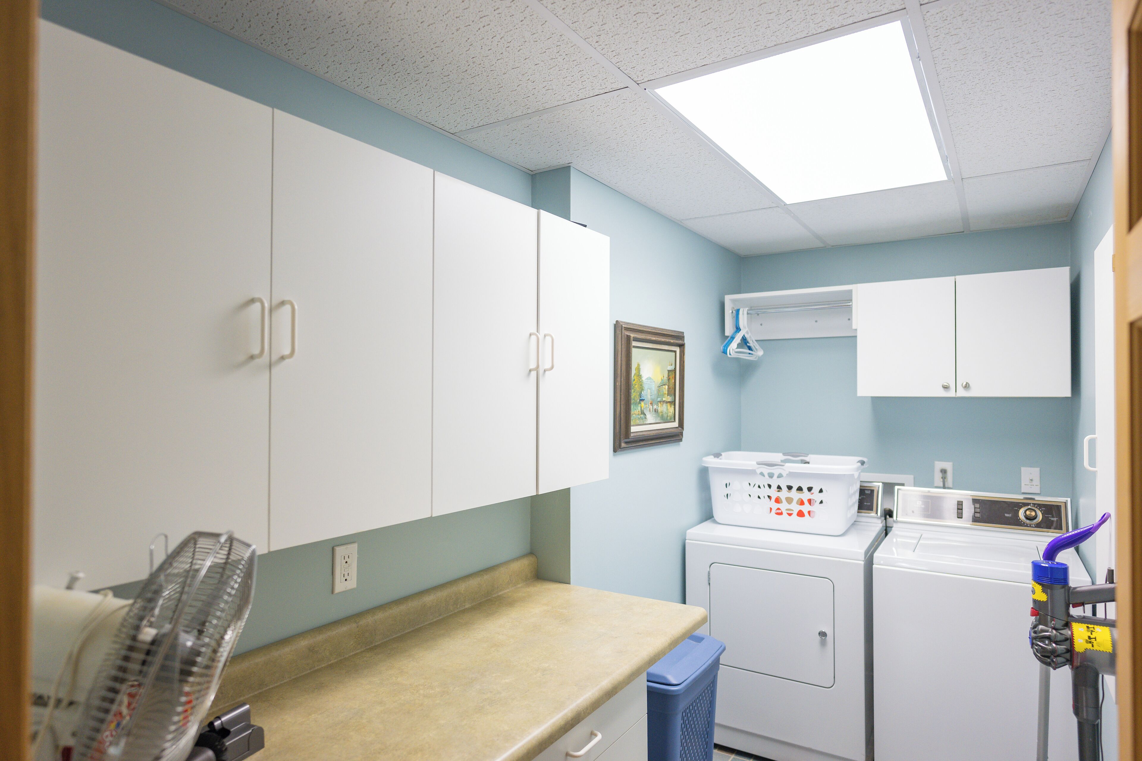 A laundry room with a washing machine, dryer, and a blue trash bin.