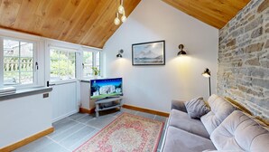 Una sala de estar acogedora con un sofá gris, un televisor sobre un mueble bajo, una alfombra estampada y una pared de piedra.