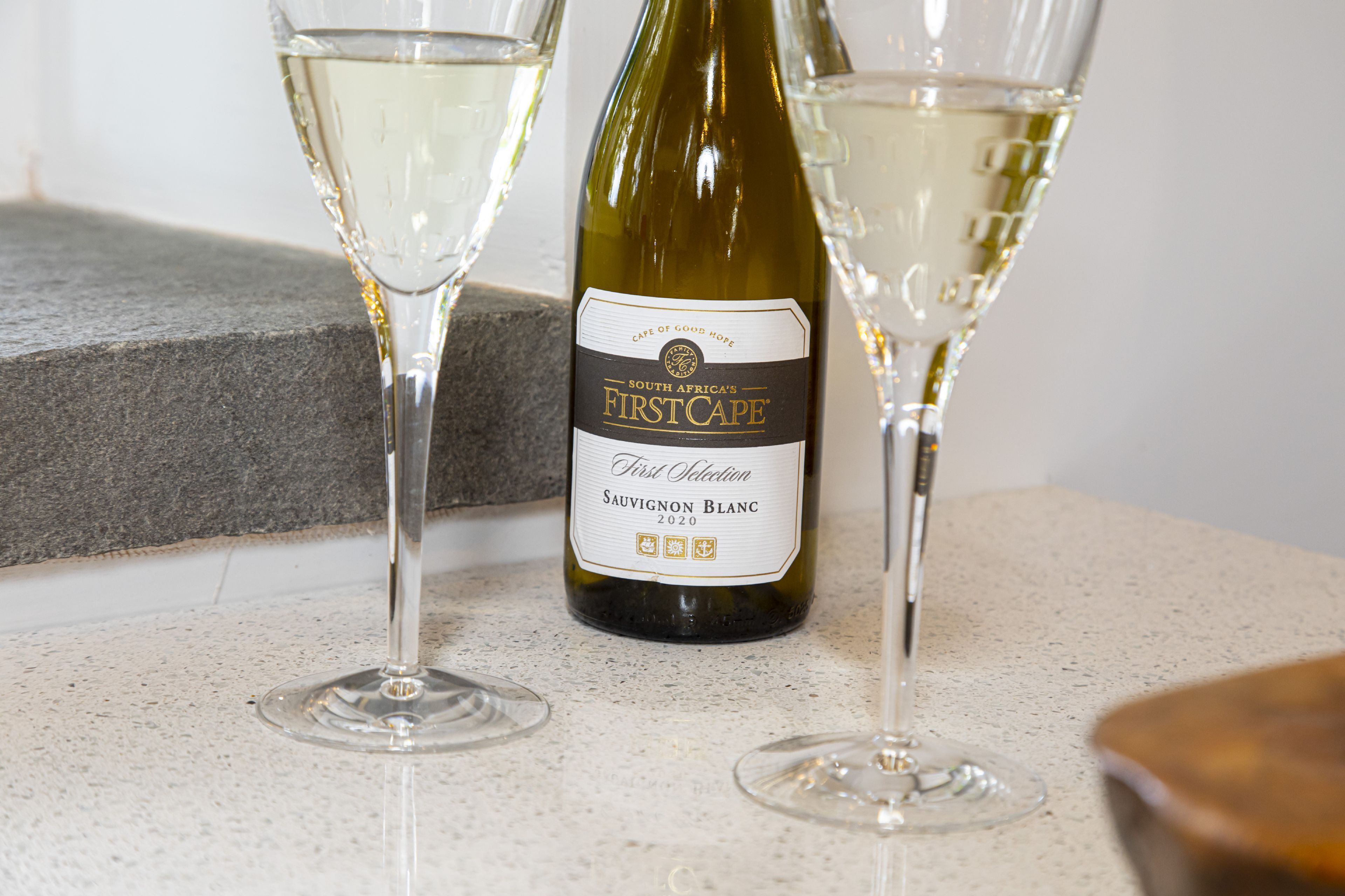 Une bouteille de vin FirstCAPE Sauvignon Blanc 2020, originaire d’Afrique du Sud, et deux verres à vin vides sont posés sur un comptoir.