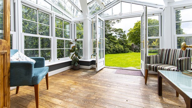 A conservatory with wooden flooring, a blue armchair, a striped armchair, and a glass table. - Yr Hen Ysgol - historic cottage in grounds of manor house (Swansea)