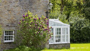 A stone building with a conservatory, surrounded by lush greenery. - Yr Hen Ysgol - historic cottage in grounds of manor house (Swansea)