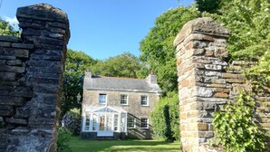 A stone house with a white windowed porch and a well-maintained lawn. - Yr Hen Ysgol - historic cottage in grounds of manor house (Swansea)