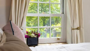 A bedroom with a large window, a bed, and a small table with a flower vase. - Yr Hen Ysgol - historic cottage in grounds of manor house (Swansea)