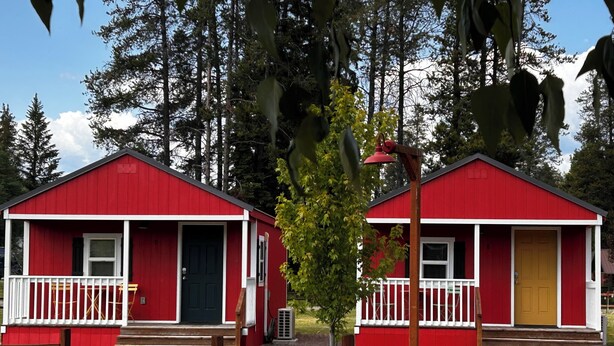 Two red cabins with white railings, a welcome sign, and a gravel path leading to them. - Cabin #9 | 10 Min to Glacier Park Entrance, Minutes to Glacier Park! (Coram)