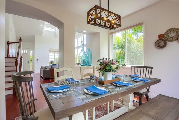A dining area with a wooden table set for four, a chandelier, and a view of the outdoors.
