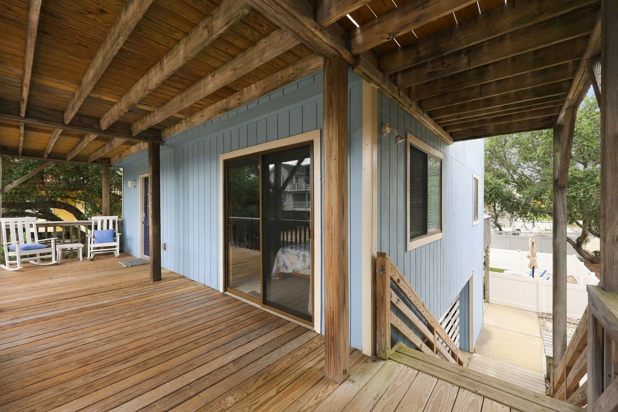 A covered wooden deck with a sliding glass door leading to a covered porch area.