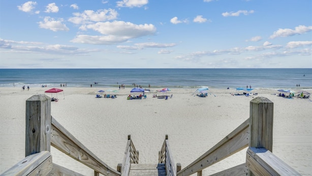Een strand met een houten trap die naar het zand leidt, parasols en strandstoelen.