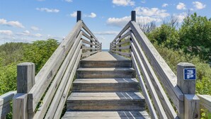 Een houten looppad dat naar een strand leidt, onder een heldere lucht.