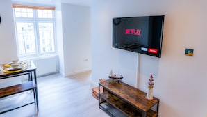 A modern living room with a flat-screen TV displaying the Netflix logo, a wooden coffee table with a ship model, and a small lighthouse decoration. - Perfect flat for the beach and town centre (Bournemouth)
