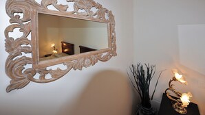 Un espejo con un marco decorativo, un jarrón con plantas y una lámpara sobre una mesa.