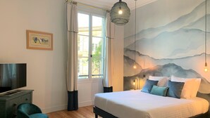 Quarto com cama, escrivaninha, cadeira, televisão e janela com cortinas.