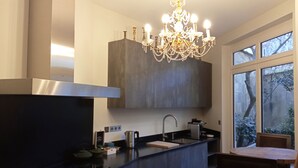 Cozinha moderna com bancada escura, coifa de aço inoxidável e lustre.