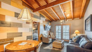 Un accogliente soggiorno con soffitto in legno, un tavolo da pranzo rotondo, un divano in pelle e un televisore.