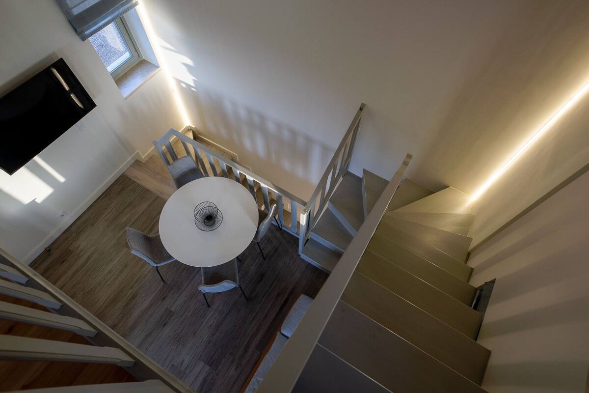 Een modern interieur met een ronde eettafel, houten vloeren en een trap met een lamp.