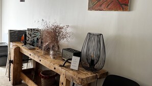 Een houten bureau met een radio, een vaas met gedroogde planten en een zwarte stoel.