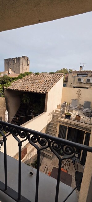 A balcony with a wrought iron railing, a view of a building with a tiled roof, and a distant castle-like structure.