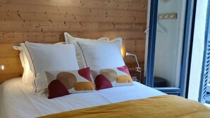 Een bed met witte beddengoed en kleurrijke kussens, een houten hoofdbord en bedlampjes.
