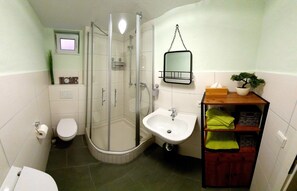 A compact bathroom with a glass-enclosed shower, a white sink, and a small shelf with toiletries.
