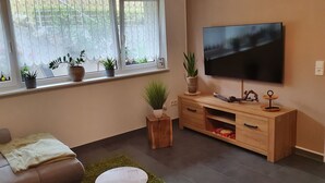 A living room with a sofa, a coffee table, a TV on the wall, and several potted plants on a windowsill. - Kaiserstuhl "auszeit " (Vogtsburg im Kaiserstuhl)