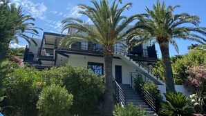 A multi-story building with a staircase leading to the upper levels, surrounded by palm trees and lush greenery. - Golfe de Saint-tropez, Villa Contemporaine Avec Piscine, vue mer et Plage à Pied (Cavalaire-sur-Mer)