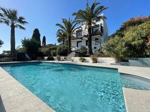 Ein Pool mit klarem, blauem Wasser, umgeben von einem modernen Gebäude mit Balkonen, Palmen und gepflegter Bepflanzung.