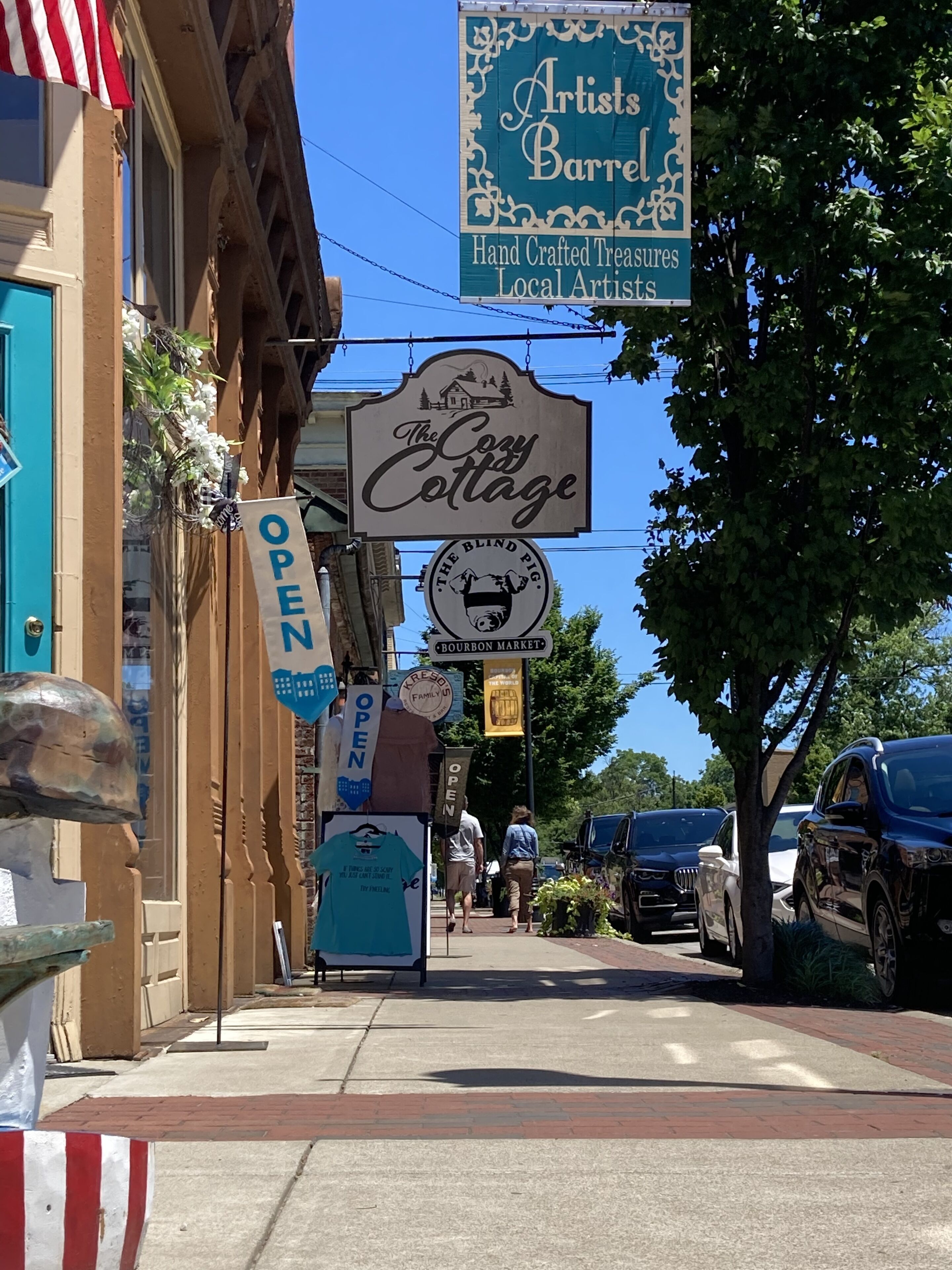 A street with various business signs, including 'Artists Barrel' and 'The Cozy Cottage.'
