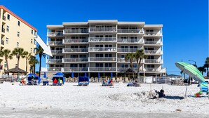Un hotel de varios pisos con balcones, situado en una playa con sillas y sombrillas.