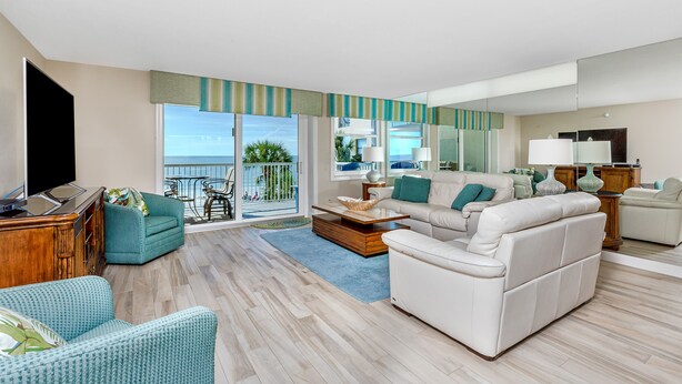 Amplia sala de estar con un sofá grande, un sillón más pequeño y una mesa de centro. Balcón con vista al mar.