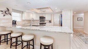Una cocina moderna con una isla central, taburetes de bar, armarios blancos y un ventilador de techo.
