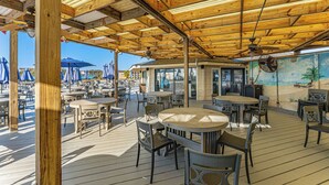 An outdoor patio with wooden tables and chairs, a ceiling fan, and a mural of a beach scene. - Folly Field Villa : Steps to Beach · Private Decks · Pool · Bikes, Golf & Dolphin Tour Included (Hilton Head Island)