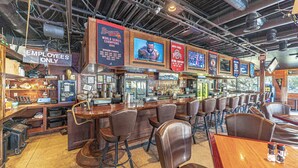 A bar area with multiple seating options, a counter, and various signs including one that says 'Brass World Series Champions.' - Folly Field Villa : Steps to Beach · Private Decks · Pool · Bikes, Golf & Dolphin Tour Included (Hilton Head Island)