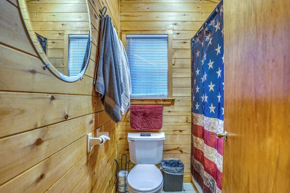 Une salle de bain avec des murs en bois, des toilettes, une fenêtre avec des stores, un rideau de douche orné d’étoiles et un porte-serviettes.