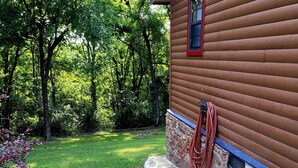 A wooden cabin with a stone foundation, surrounded by a well-maintained lawn and dense trees. - The Patriot Cabin close to the Buffalo National Park and River! Sleeps 4! (Harriet)