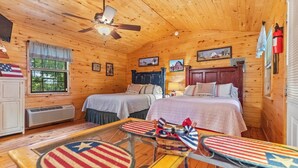 A cabin-style room with two beds, a ceiling fan, a window with curtains, and a table with American flag-themed tablecloths. - The Patriot Cabin close to the Buffalo National Park and River! Sleeps 4! (Harriet)